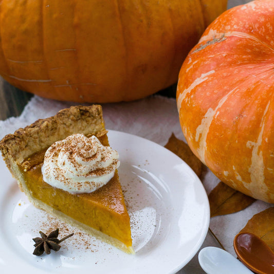 Pumpkin pie slice with whipped cream on a plate, surrounded by pumpkins and autumn leaves.