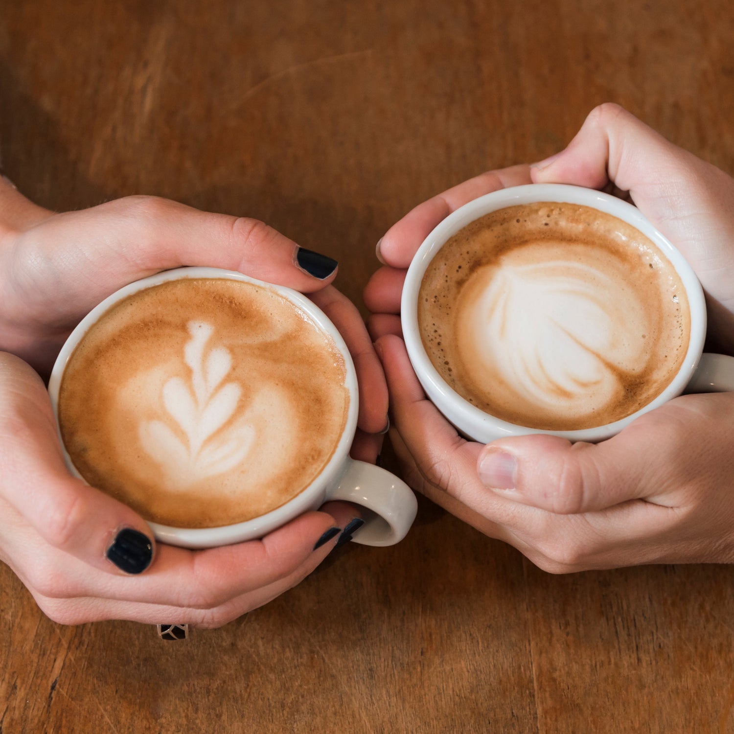 Two hands holding latte art cups showcasing 12 oz. Double Delight coffee duo from Pneuma Java. Perfect for customizing your East African coffee pair.